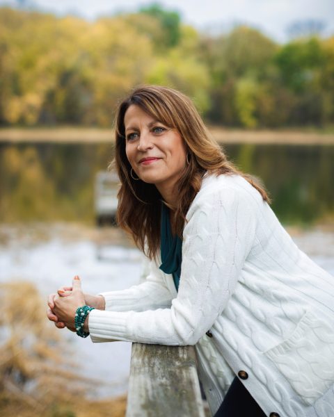 ស្ត្រីម្នាក់ផ្អៀងលើរបាំងឈើក្នុងបរិយាកាសធម្មជាតិ ដោយមានទឹកនៅផ្ទៃខាងក្រោយ