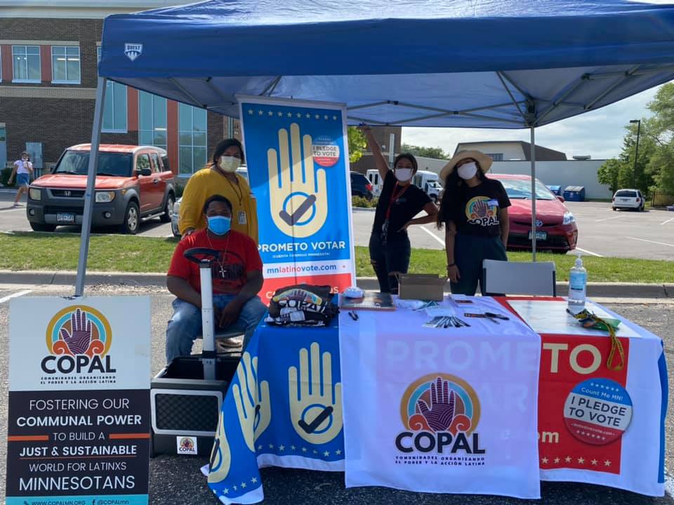 4 people standing behind a table with voter engagement posters