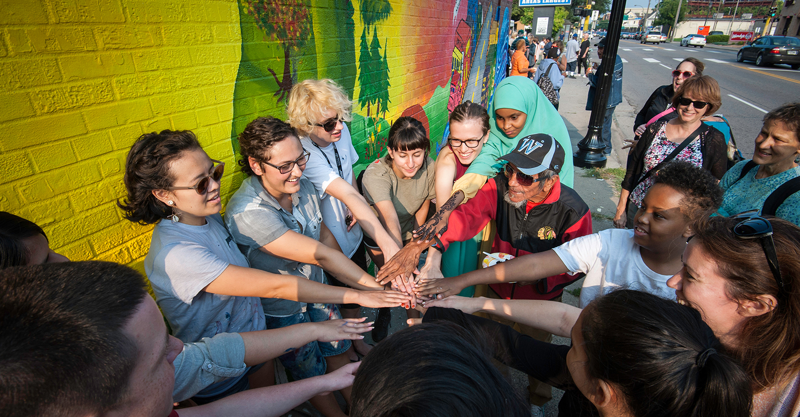 Group of people joining hands in front of a mural