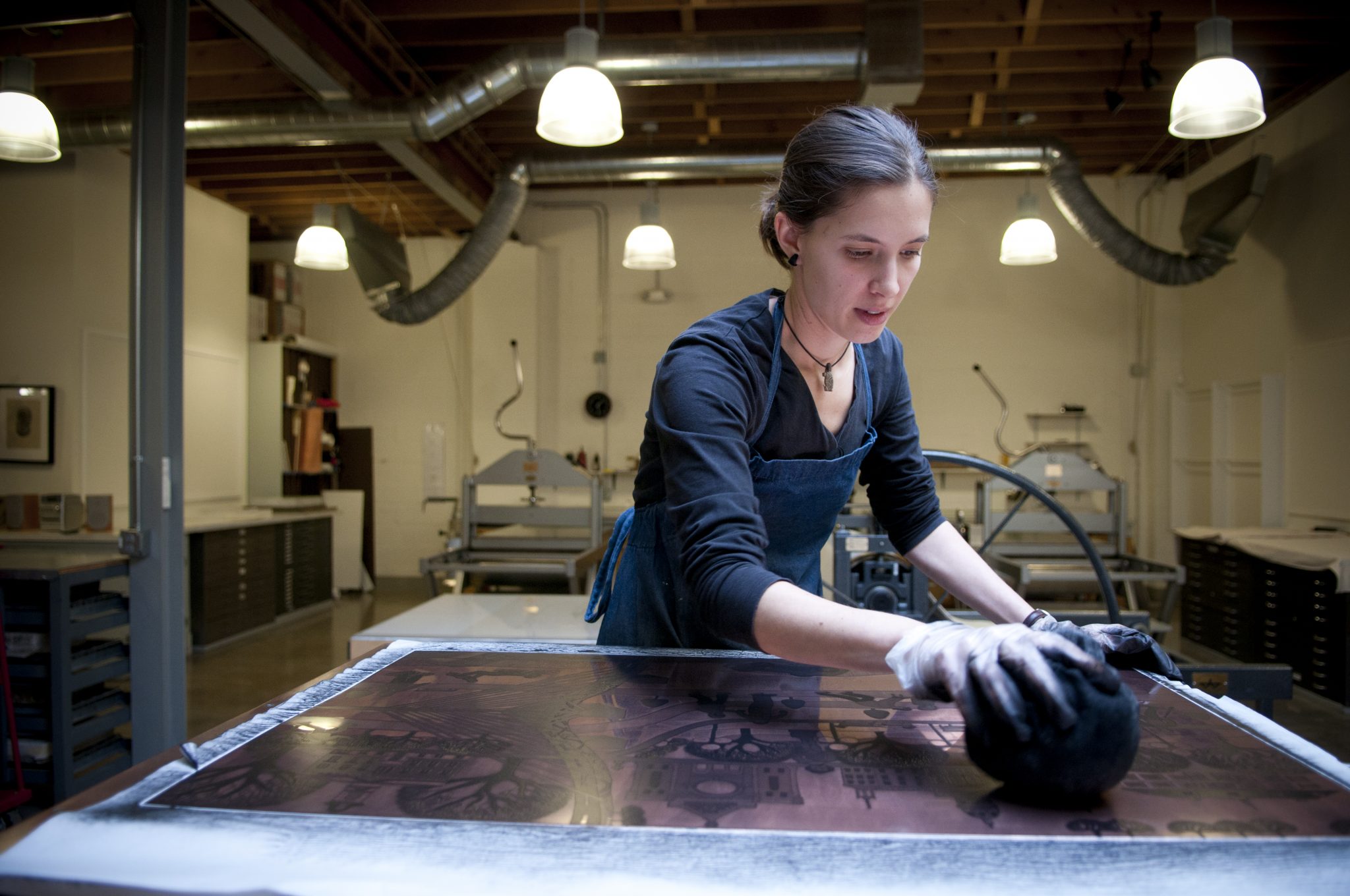 Co-op artist Miriam Rudolf wipes ink on an etching plate, preparing it so she can print on the press.