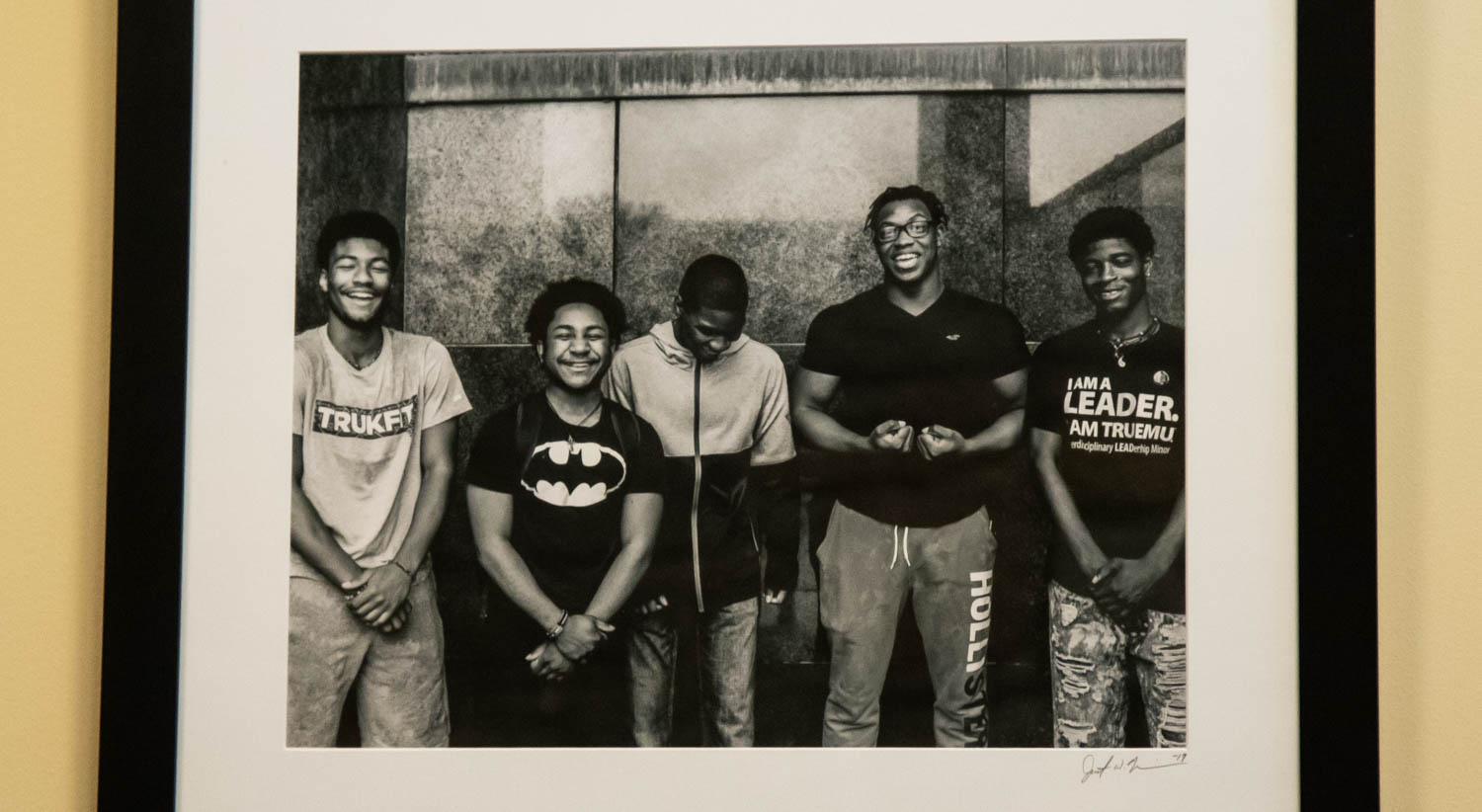 A black and white photograph that shows five young black men smiling and laughing