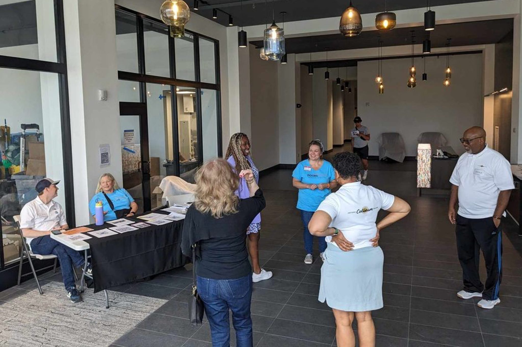 Eight people in a building lobby. Two sit at a folding table handing out informational materials.