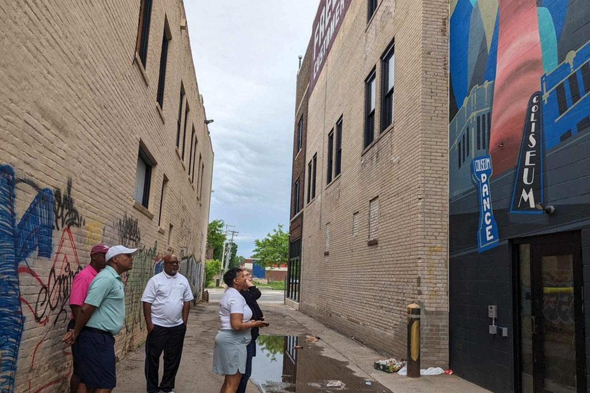 Five people admire a large colorful mural honoring the historic coliseum's legacy, featuring marquee signs that say "Coliseum DANCE" and "COLISEUM"