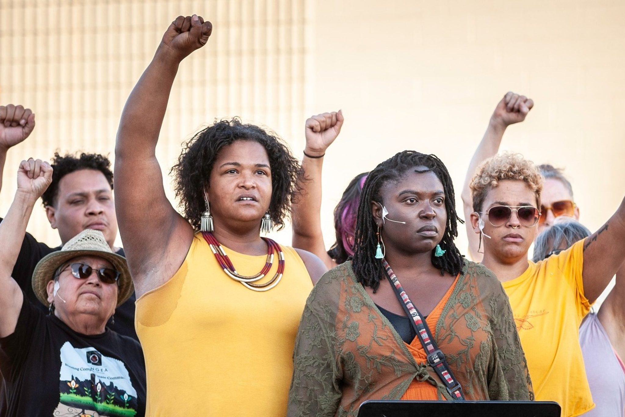 A multiracial group of 8 people stand with raised fists